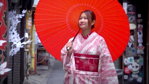 快乐年轻美丽的亚洲女性穿着传统的日本和服手拿红纸伞微笑着走在日本东京新宿地区的街道上