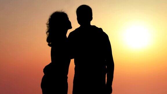 剪影的年轻女子亲吻她的男朋友享受美丽的日落