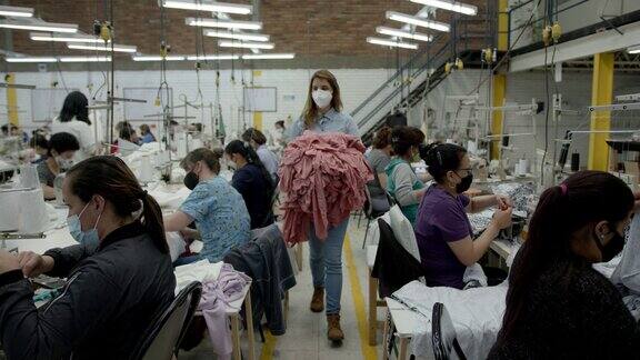 纺织厂的年轻女工人提着衬衫走在生产线上
