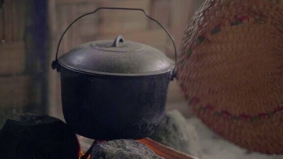 在篝火上用扇子吹火做饭在传统的亚洲村落里在火锅里烧柴火准备晚餐