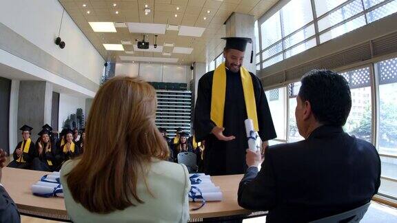 一个自豪的男学生在毕业典礼上接受他的大学文凭而他的同学们都兴高采烈地鼓掌