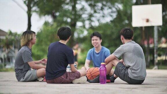 亚洲的中国少年篮球运动员在篮球场上喝着水和朋友们在比赛后坐在地上休息