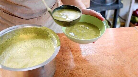 厨师从平底锅中向碗中倒入一碗绿色菠菜奶油汤