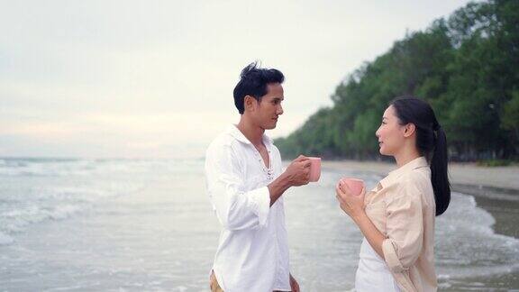 年轻的亚洲夫妇早上在热带海滩一起喝咖啡