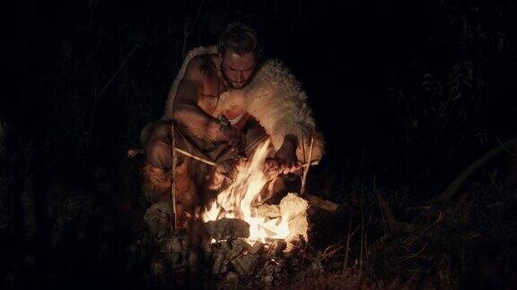 一个披着兽皮的大胡子男人晚上在乡下在火边休息吃苹果晚上在火边吃东西的野蛮人