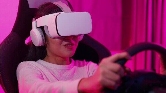 年轻的亚洲玩家坐在驾驶模拟器赛车模拟器戴着虚拟现实眼镜四维屏幕享受玩游戏的乐趣在家里的游戏室粉红色的霓虹灯在晚上