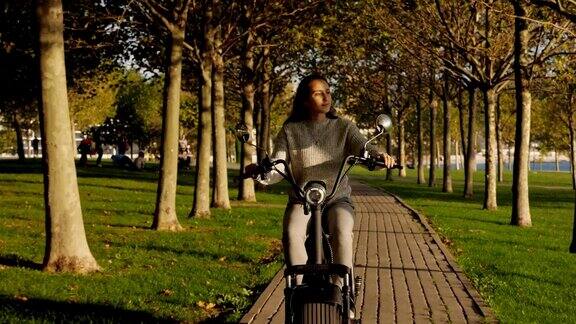在阳光明媚的早晨小女孩骑着电动车穿过公园