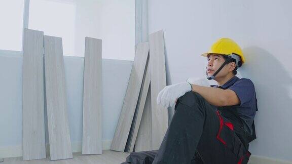 亚洲建筑工人男下班后去装修房子感到很累工匠建筑工人或木匠工人戴黄色劳动安全安全帽在室内安装层压板后铺设地板