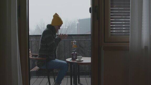 在寒冷的日子里年轻女子坐在阳台上用野营炉准备咖啡