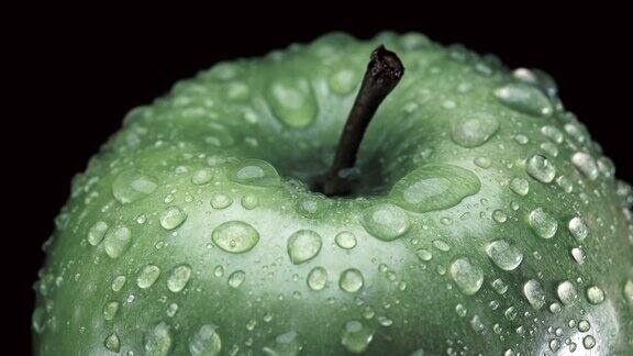美丽的绿色苹果与水滴旋转的黑色背景特写