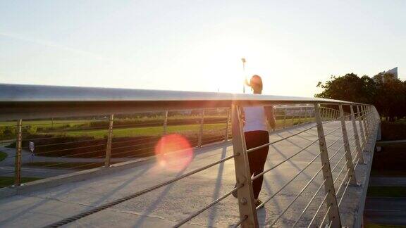 慢镜头:在阳光明媚的早晨运动女子在城市的桥上慢跑