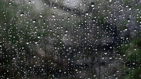 雨落在窗外绿树成荫的玻璃上特写镜头缓慢的运动雨水打在玻璃上雨滴落在车窗背景上