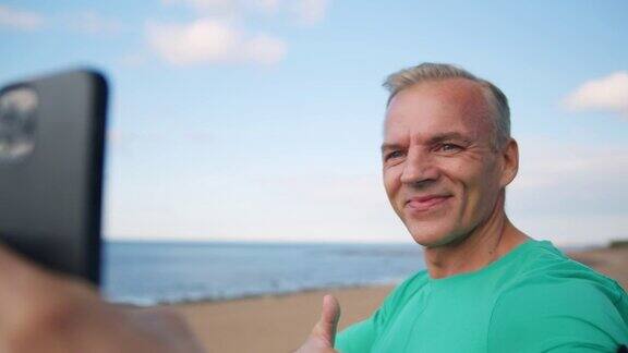 一个身材健美的金发斯堪的纳维亚男人正在用手机自拍微笑着竖起大拇指