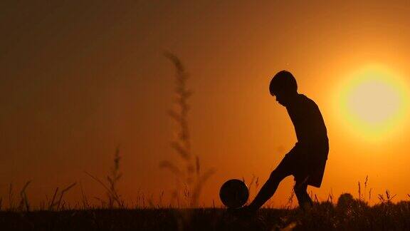 一个男孩在日落时踢足球的剪影日落时分一个男孩在操场上颠球