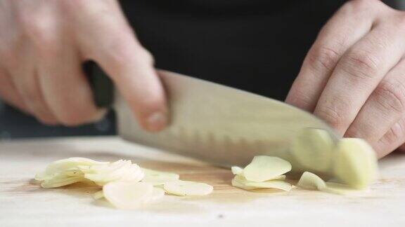 厨师长正面用刀将生姜切成薄片放在砧板上