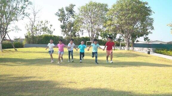 在阳光明媚的夏日一群快乐的亚洲幼儿园小朋友穿着休闲服装手牵着手在公园里玩耍、奔跑