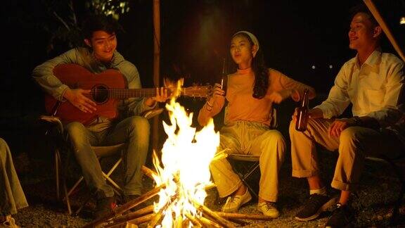 一群快乐的亚洲朋友弹吉他唱歌享受野营和玩烟花