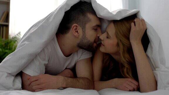 温柔的情侣在毯子下接吻幸福的新婚夫妇享受蜜月爱