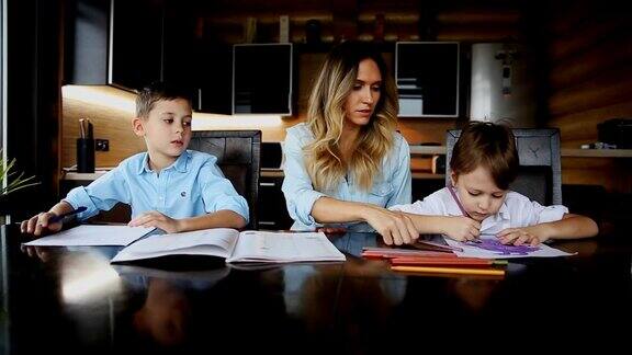 快乐的家庭两个孩子的母亲帮助儿子做他们的家庭作业坐在厨房的大桌子