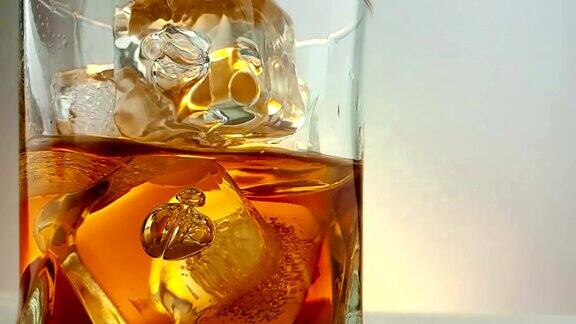 特写的酒保倒威士忌在饮用玻璃与冰块在温暖的白色背景时间放松喝威士忌