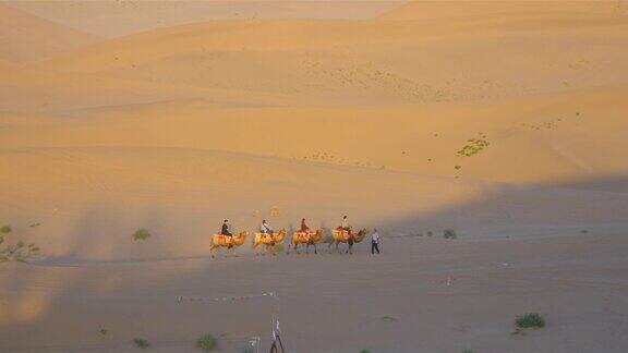 美丽的黄昏景观的沙漠和骑骆驼的人在甘肃敦煌中国