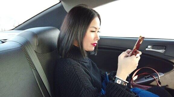 亚洲妇女在汽车后座上使用手机