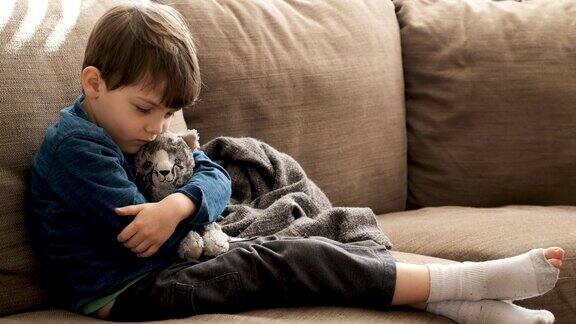 严肃沉思的小男孩抚摸着他的毛绒玩具猫