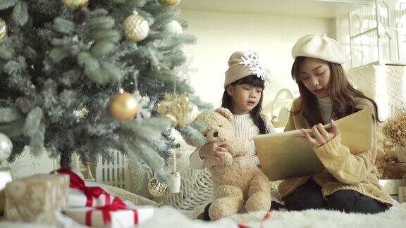 4K可爱的小女孩和妈妈在圣诞树旁看书