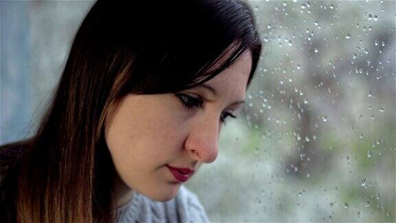 悲伤的年轻女子心不在焉地坐在潮湿的窗户旁近距离
