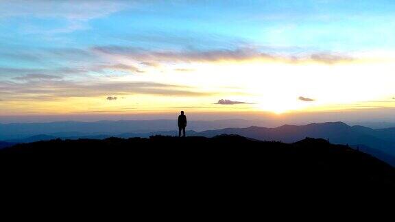 在日出的背景下快乐的人站在山上