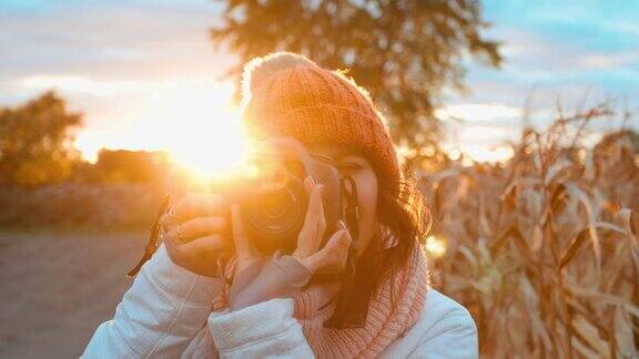 美丽的年轻女子与数码相机照片在日落