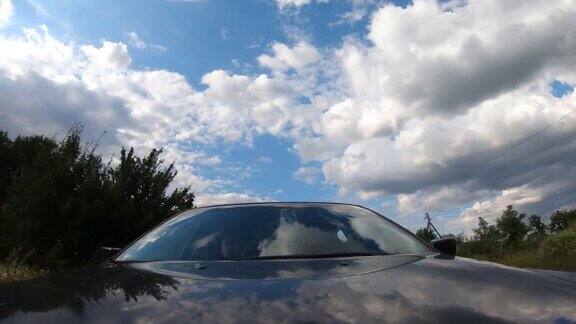 一辆黑色的汽车在乡间行驶车盖和车窗上反射着阴云密布的天空沿着高速公路驾车穿越美丽的风景从挡风玻璃上的引擎盖看