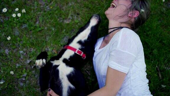 一个快乐的女人躺在草地上和她的狗玩