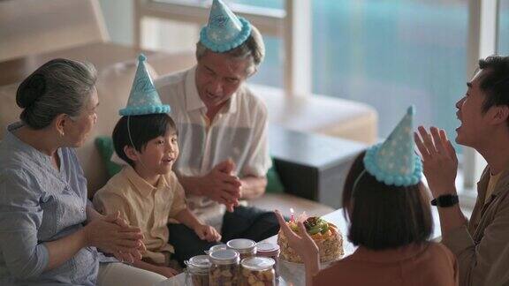 亚洲华人多代同堂在客厅拍手唱生日歌庆祝6岁男孩的生日