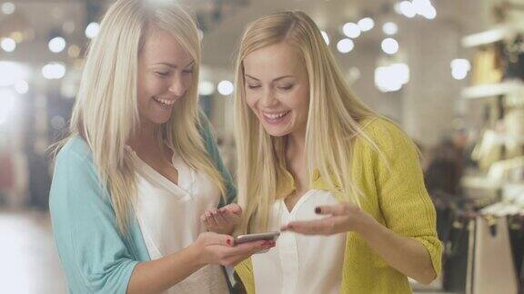 两个开朗的金发女孩在一家百货商店里使用智能手机