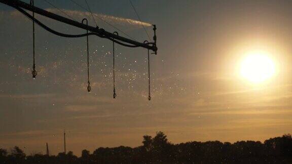 农业灌溉灌溉系统农田自动人工灌溉系统日落时在背光下飞溅的水珠在阳光下闪闪发光