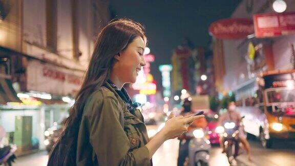 亚洲美丽的女人背包客滚动手机而走在城市有吸引力的女孩旅游旅行者独自在街上旅行使用智能手机享受假期假期旅行的时间在夜间道路