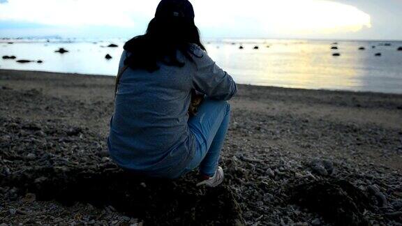 悲伤的女孩坐在日落的海滩上