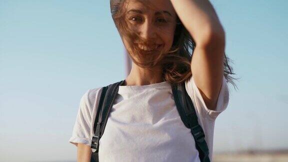 身穿白色t恤的年轻漂亮女子站在桥上在蓝天的背景下笑着享受着宁静的日落看着相机
