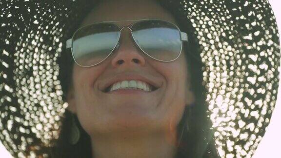 戴着帽子看大海的快乐女人透过她的太阳镜看到的倒影