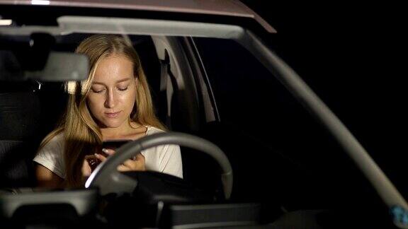 微笑的女人晚上在车里用智能手机