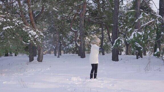 快乐可爱的女孩穿着温暖的冬衣蹦蹦跳跳玩得开心还扔雪下雪的冬天在阳光明媚的日子里在新鲜的霜冻空气中享受乐趣美丽的背景积雪的自然松树林慢动作