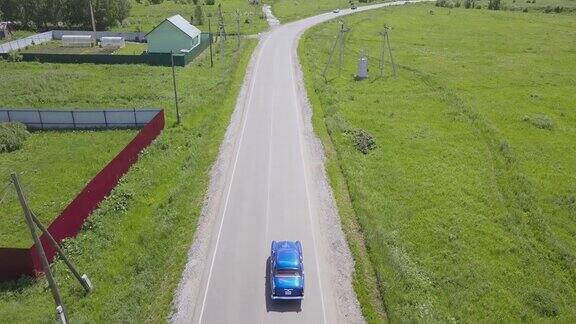 从无人机上看蓝色复古的俄罗斯汽车在村庄的道路上行驶