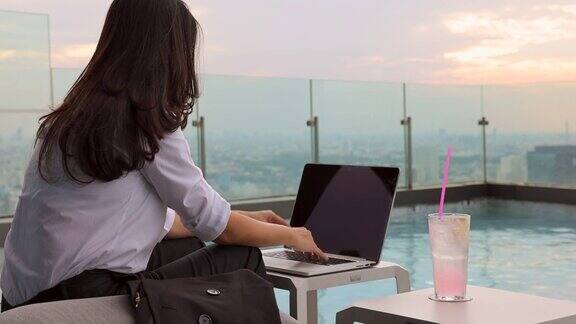 夏日生活方式亚洲妇女放松和chill附近的豪华游泳池摩天大楼一个亚洲女人在笔记本电脑上工作模糊的背景摩天大楼美丽的天空