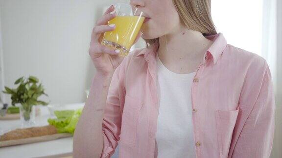 不认识的可爱女孩喝着橙汁对着镜头微笑年轻的白人女人享受美味的有机饮料广告健康的生活方式幸福