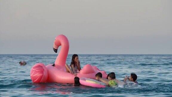 暑假小孩子们在海上玩粉红色的充气火烈鸟