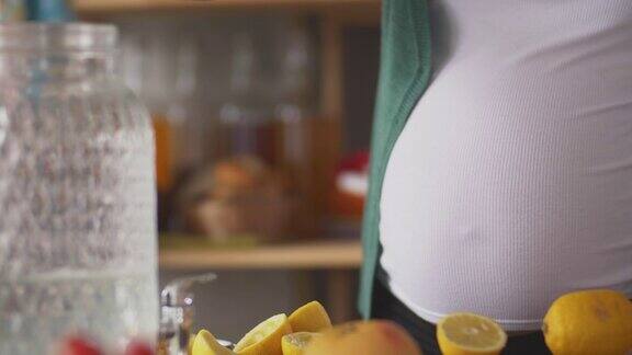 孕妇的腹部挤压和倒新鲜柠檬汁到玻璃水罐