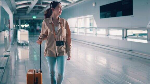 幸福微笑的亚洲女旅客走在机场候机楼行李箱行李