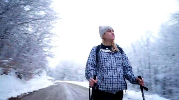 女性徒步旅行者走在积雪的森林旁的道路上