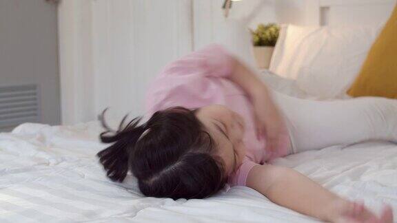 年轻的亚洲女孩在家里醒来后玩亚洲日本妇女孩子在床上躺了一晚上后放松休息乐趣在早上在家里的卧室里感到舒适和平静缓慢的运动